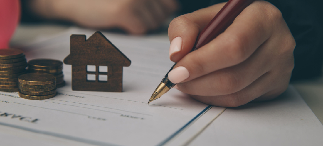 persona firmando un papel en el que aparece una casa y dinero en efectivo